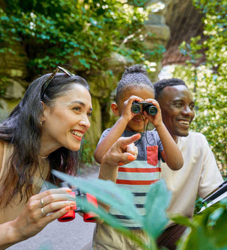 Family outdoor adventure, with a young boy using binoculars, alongside smiling adults, observing nature at Glen Span Arch in Central Park.