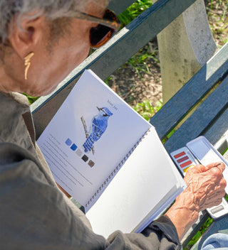 Person sitting on a park bench with a watercolor book, painting a blue jay while enjoying a quiet moment in Central Park.