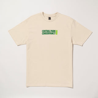 Sand colored t-shirt with A 'Central Park Conservancy' Pentagram designed logo printed mid chest on a gray background.