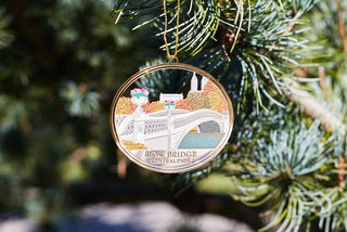 a stamped metal ornament  of Bow Bridge hangs on an evergreen bough