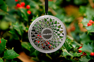 Silver decorative ornament with 'IMAGINE' text hanging on a green leafy background