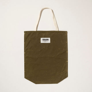 Olive green waxed canvas tote bag with antique brass snaps and  a beige woven label of the Central Park Conservancy logo on a light gray background