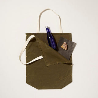 Olive Green waxed canvas  tote bag with a blue bottle and a scone on a light gray background